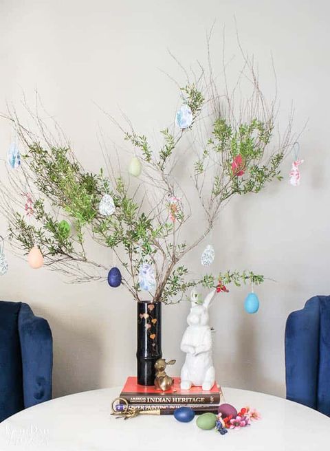 easter tree made out of spring sprigs sitting on books on a table with a white ceramic bunny sitting next to it