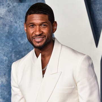 usher smiles at the camera, he wears a white asymmetrical suit jacket with a necklace peeking out