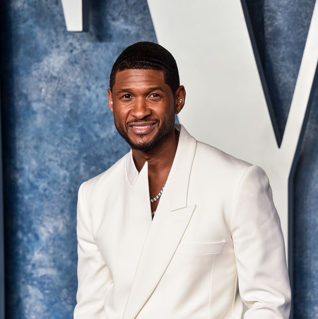 usher smiles at the camera, he wears a white asymmetrical suit jacket with a necklace peeking out