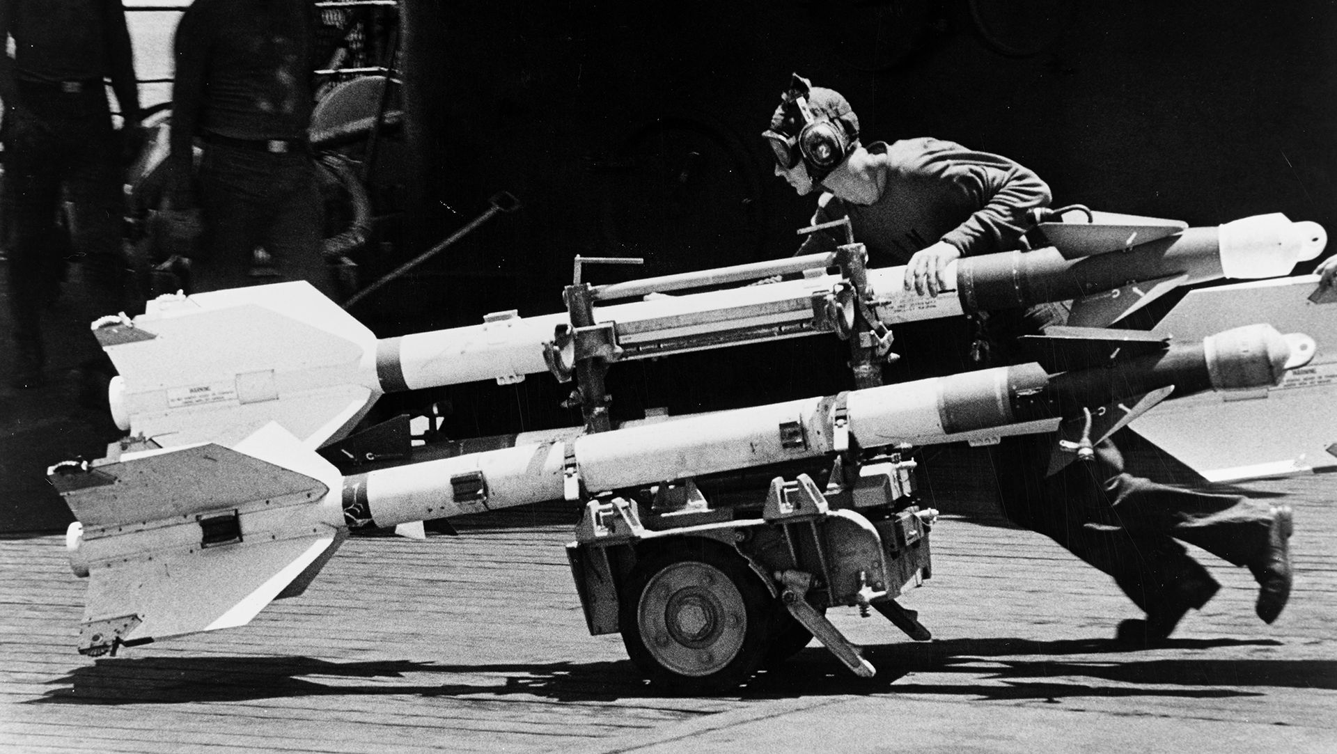 a crewman wheels a cart loaded with three sidewinder airtoair guided missiles across the flight deck, during operations off vietnam in april 1967