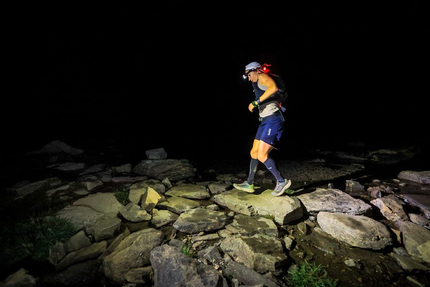 a woman running over rocks in the dark at the 2024 utmb