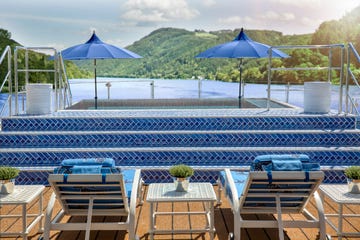 an outdoor pool area overlooking a scenic landscape featuring blue umbrellas and loungers