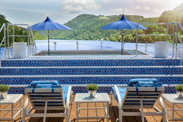 an outdoor pool area overlooking a scenic landscape featuring blue umbrellas and loungers