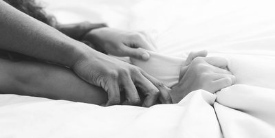 black and white focus couple gripping wrists and hands in bed on white sheets