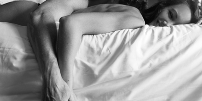 couple cuddling on bed in black and white focus smiling face down on white sheets