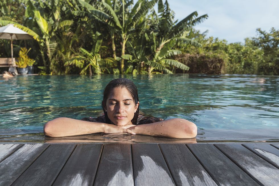 horizontal serene woman sunbathing at paradisiacal infinite pool resort with palm trees in lombok island people lifestyles in indonesia