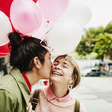 man kissing smiling girlfriend on cheek while giving her balloons during date
