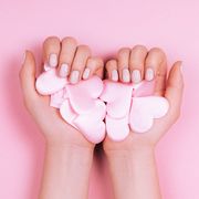 pink hearts confetti in female hands with elegant manicure on pastel background flat lay style