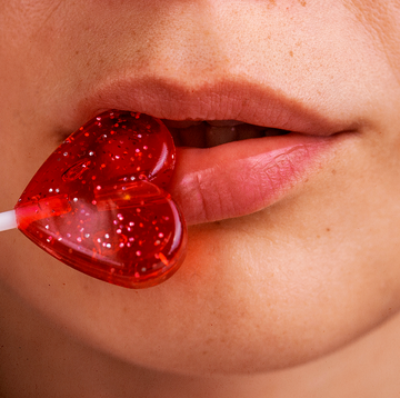 close up of a heart shaped lollipop against lips