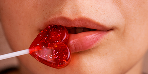 close up of a heart shaped lollipop against lips