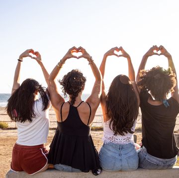four girls sitting and holding up hands into hearts while looking out on the beach