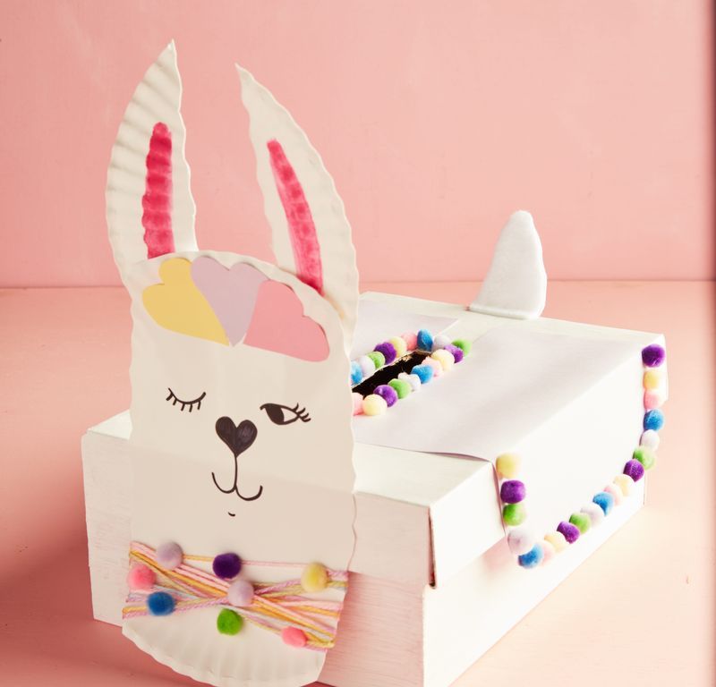 llama valentine box idea with paper plate face, decorated with colorful mini pom poms, yarn, paper cutouts, and markers