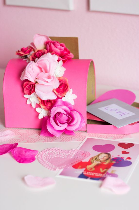 pink cardboard mailbox decorated with a band of faux flowers with valentine's day cards inside