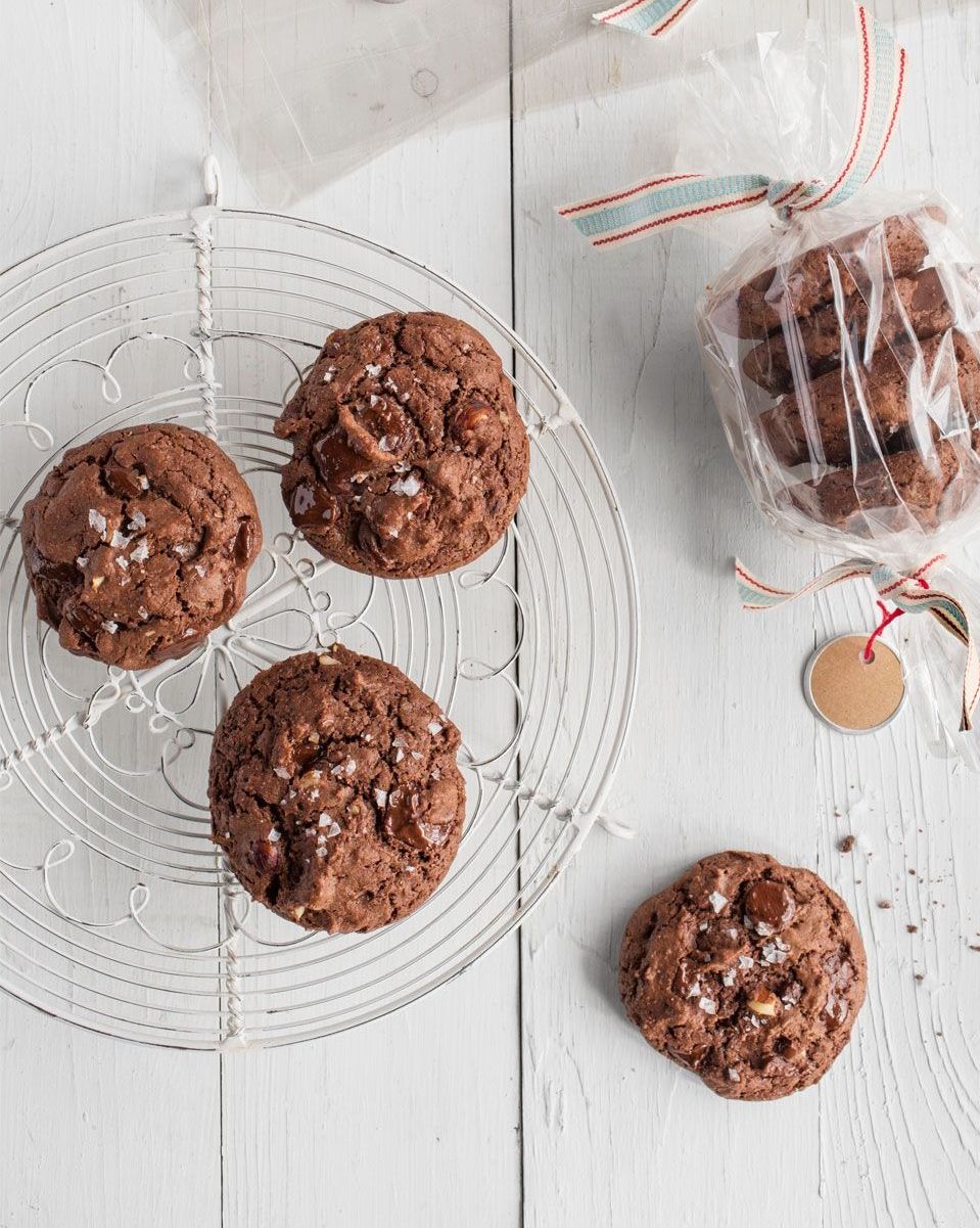 triple chocolate hazelnut cookies on a wire rack and also stacked in a plastic gift bag tied with ribbon