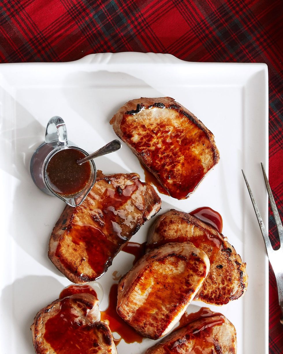 pork chops with bourbon molasses glaze on a white serving plate with a small cup of additional glaze