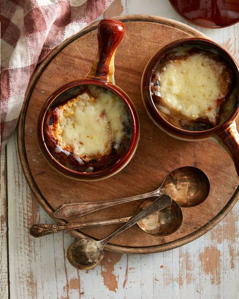 classic french onion soup in brown crocks with old vintage spoons next to them