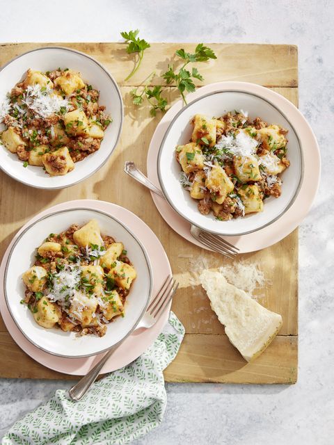 potato gnocchi with pork ragu in bowls with grated parmesan and freshly chopped herbs on top