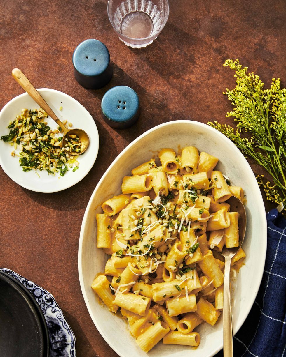 creamy pumpkin pasta in a large white oval serving plate with pine nut gremolata and a gold spoon for serving