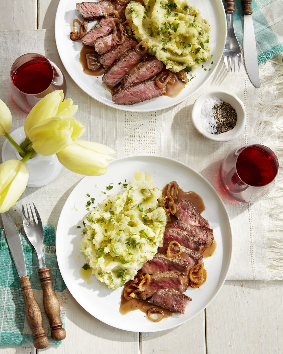 strip steak with lemon mashed potatoes on a white plate with silverware and a glass of wine