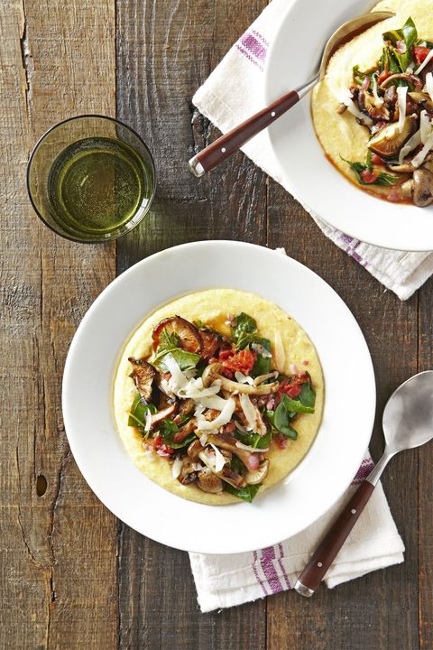 creamy polenta with mushrooms and collards in a white bowl with a spoon