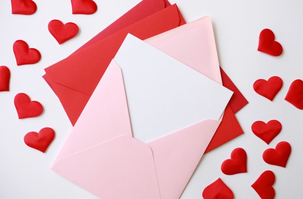 red and pink envelopes for valentine's day cards on a table, surrounded by scattering of red paper hearts