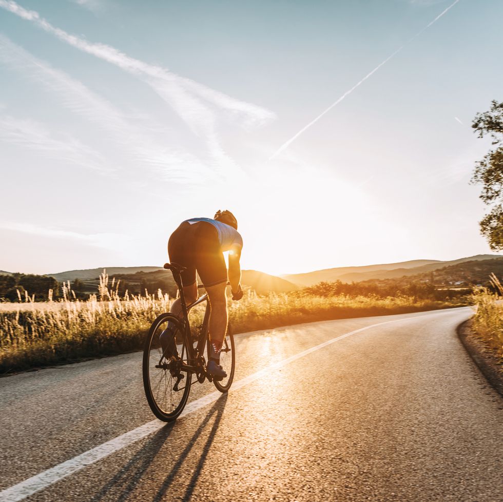 cyclist riding on a road with the sun setting