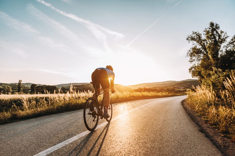 cyclist riding on a road with the sun setting