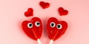 two red heart lollipops with funny googly eyes looking at each other and several smaller red hearts