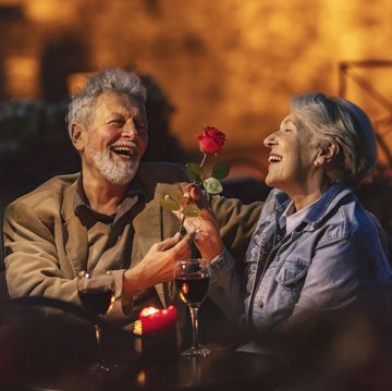 lovely old lady admiring the red flower that her husband gave her while the two have glasses of red wine at a restaurant at night