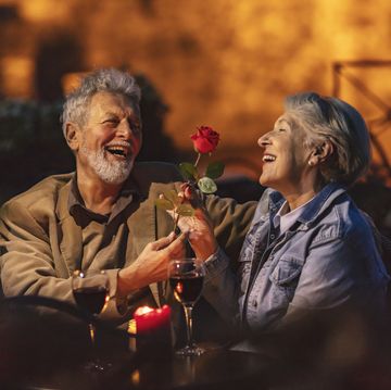 lovely old lady admiring the red flower that her husband gave her while the two have glasses of red wine at a restaurant at night