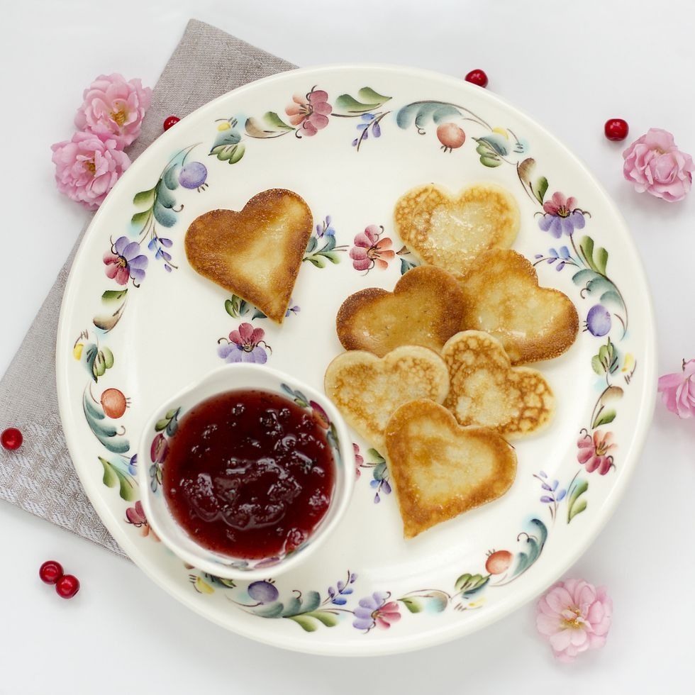 mini heart shaped pancakes on floral plate with jam, garnished with pink flowers