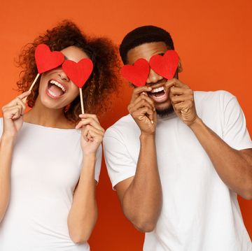 lovers blinded by their big love young cheerful african american couple in love holding red hearts over eyes and smiling, orange background