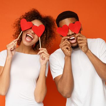 lovers blinded by their big love young cheerful african american couple in love holding red hearts over eyes and smiling, orange background