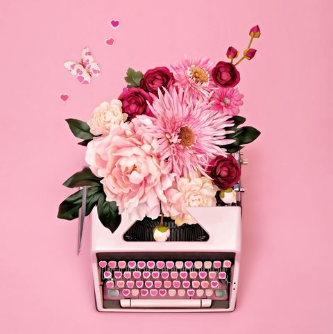 overhead view of vintage pink typewriter with candy heart keys and flowers, butterflies, and hearts spilling from paper return on pink background