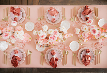 overhead view of pink and white flowers arranged on a pink tablecloth with pink and white dinnerware
