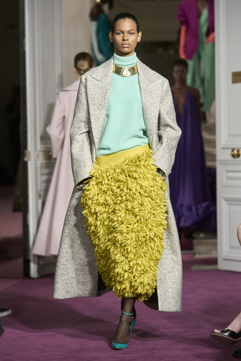 a model wears a long coat and a chartreuse bubble skirt