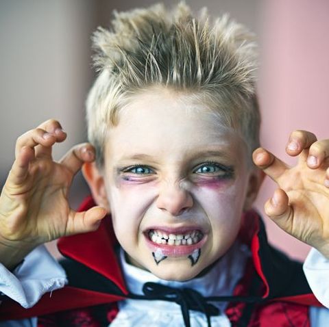 a blonde headed boy with teeth snarled and dressed up like a vampire for halloween