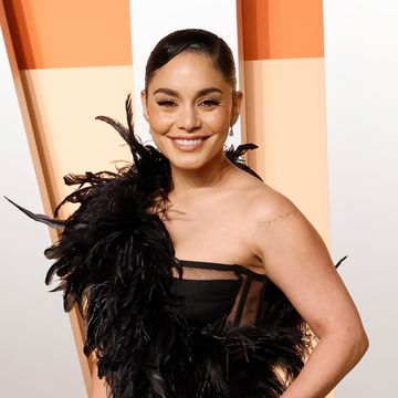 a woman in a black gown with feathers and one shoulder strap smiles at the camera