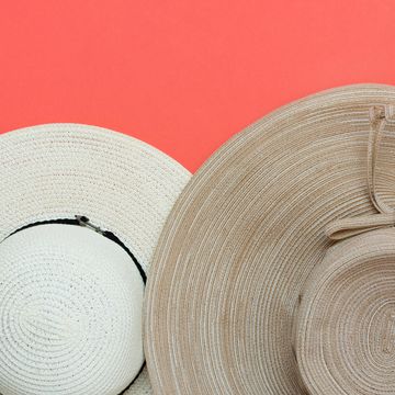 Various broad brimmed women's straw hats on trendy coral pink background. Summer vacation fashion accessories beach party concept. Top view flat lay. Minimalist elegant style. Copy space