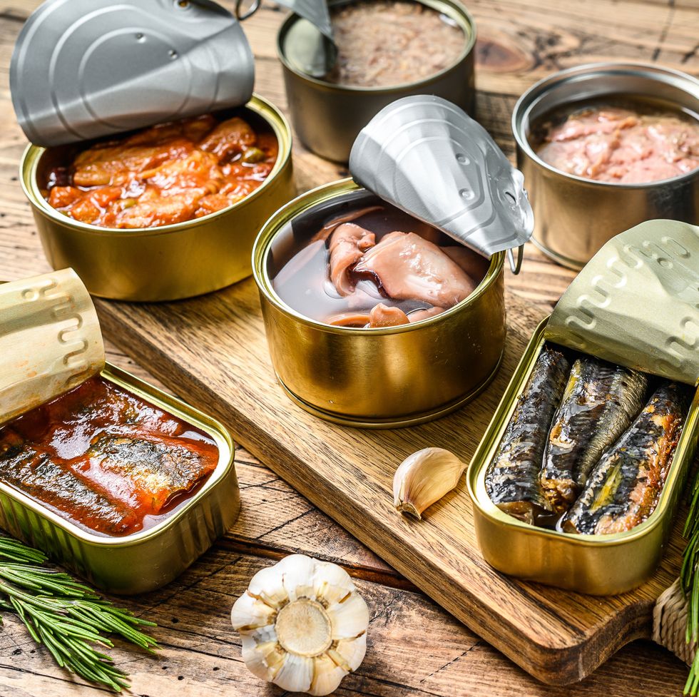 various canned  fish and seafood in a metal canswooden background top view