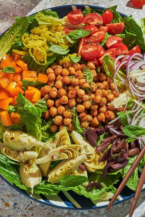 vegan antipasto salad with artichoke hearts, kalamatas, red onion, tomatoes, pepperoncinis, orange peppers, and chickpeas atop romaine in a blue and white striped bowl