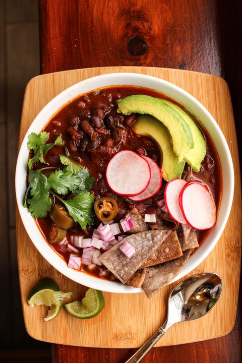 chunky vegan black bean soup in a white bowl, topped with pickled jalapeños, radishes, avocado, red onion, and tortilla chips