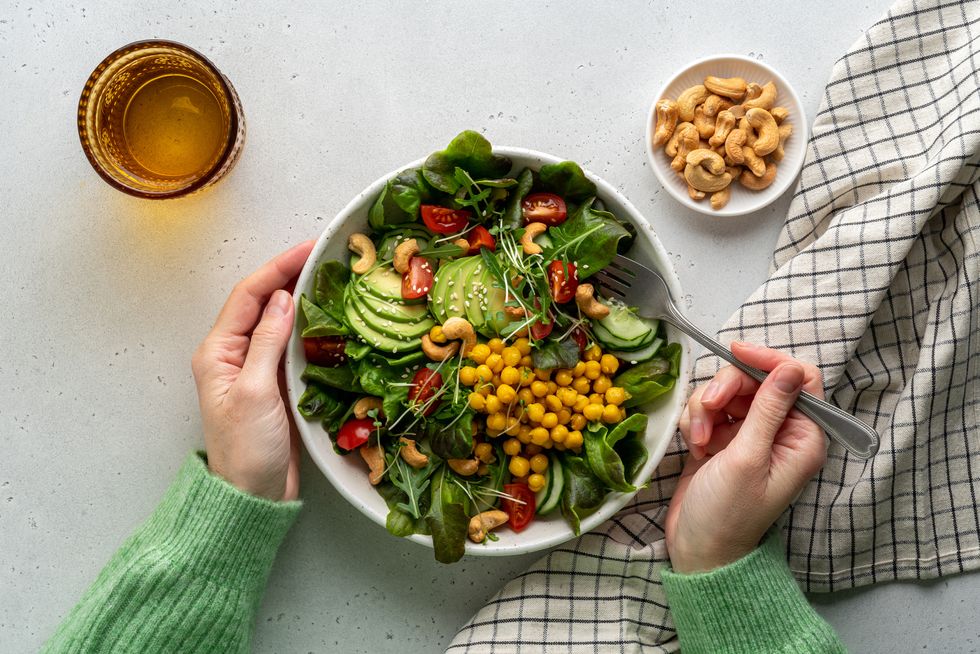 anonymous female dining healthy vegan plant based salad in bowl with avocado, cashew, micro greens, pok choi, chickpeas, tomato, lettuce, cucumber, sesame flexitarian fatty acids and dietary fiber