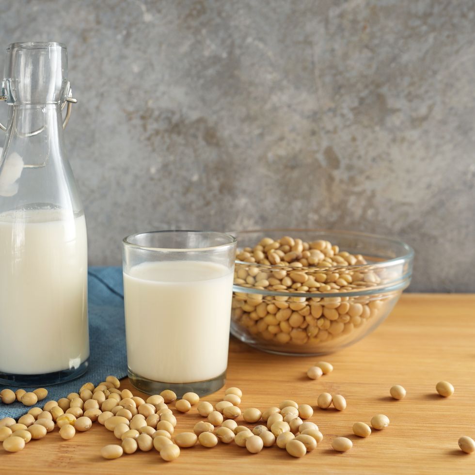 vegan soy milk in a bottle and a drinking glass and soybeans in a bowl on a wooden table against a rustic wall, alternative to animal dairy products, copy space