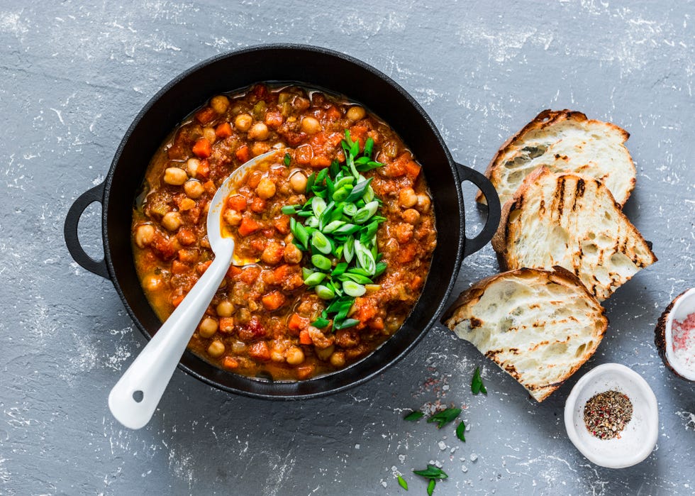 Healthy Carbs: Vegetarian mushrooms chickpea stew in a iron pan and rustic grilled bread on a gray background, top view. Healthy vegetarian food concept. Vegetarian chili