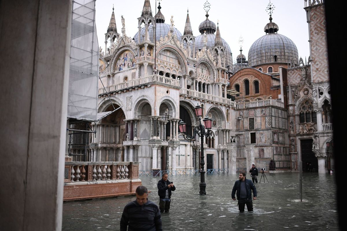 Voetgangers met lieslaarzen steken het overstroomde San Marcoplein in Veneti over Door uitzonderlijk hoogwater stortbuien en de windrichting in dit jaargetijde is de huidige waterstand de hoogste in vijftig jaar