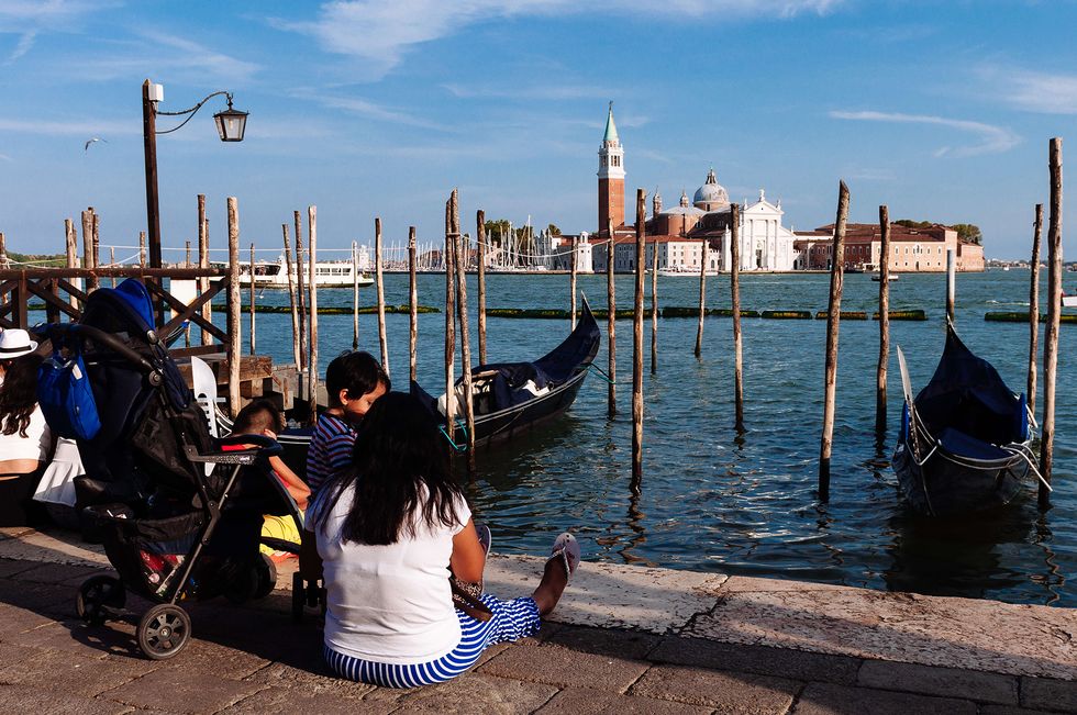 Tourists sit on the ground in Venice while looking over the Church of San Giorgio