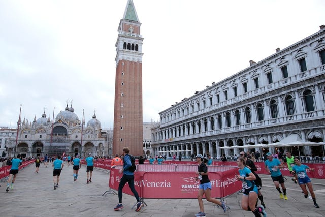 a group of people running on a track in front of a large building with piazza san marco in the background