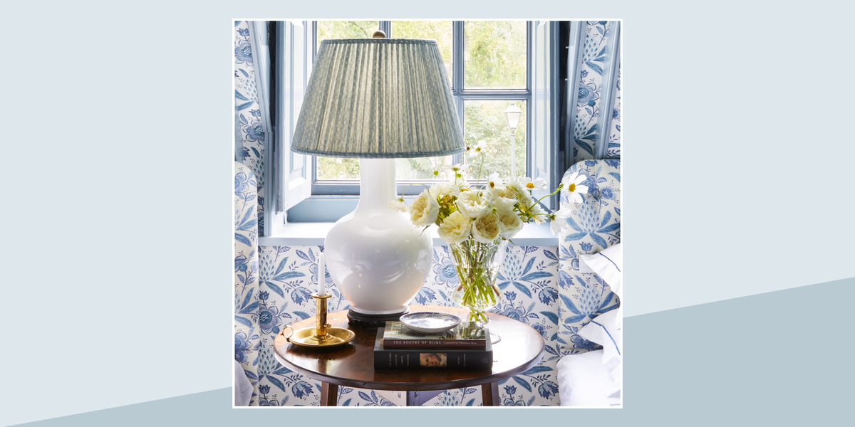 a white lamp on a table with a light blue pleated lampshade and flowers and other accessories on the table too