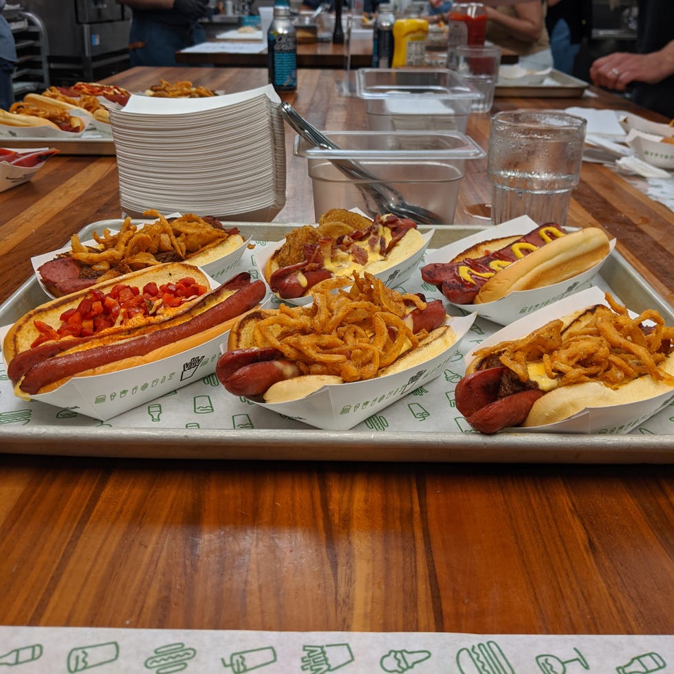 six hot dogs on a tray loaded with assorted toppings